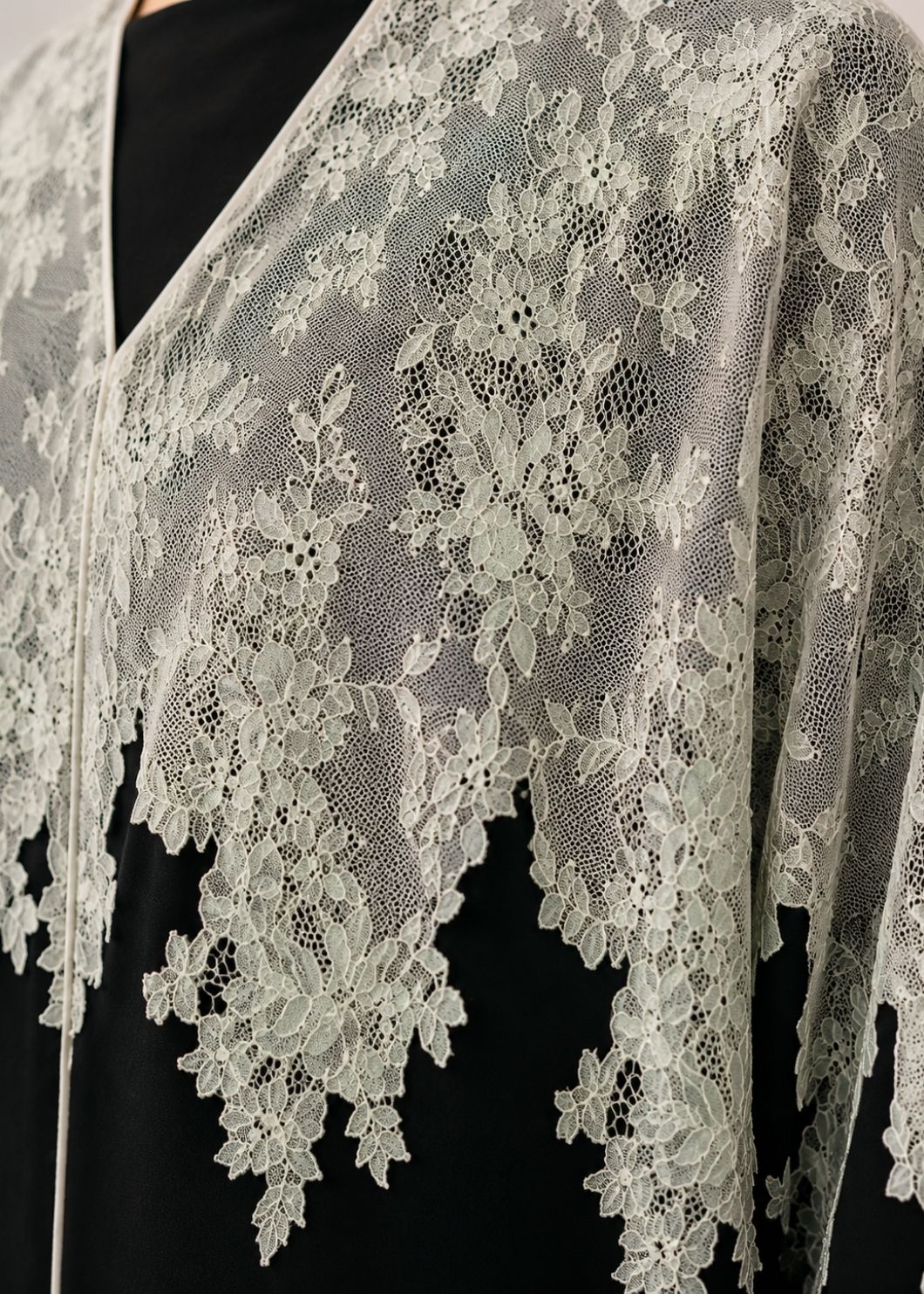 Close-up of a white floral lace shawl draped over a black dress, showing the intricate lace pattern and scalloped edges.